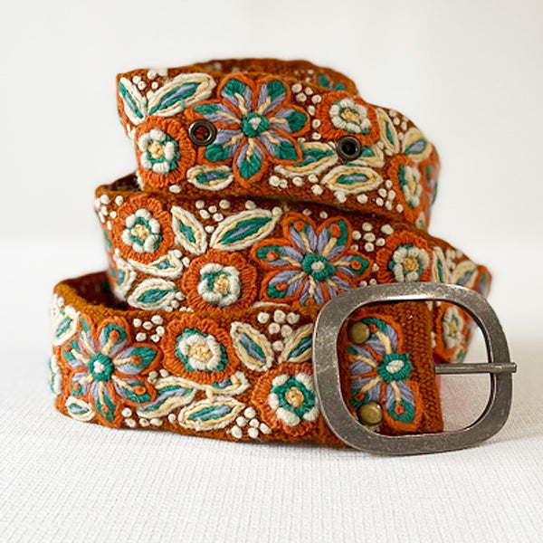 Photo of colorful hand-embroidered floral wool belt by Jenny Krauss, made in Peru with lead-free metal buckle. Versatile design with five sets of 2" spaced holes for hip or waist wear, featuring slight stretch for comfort.