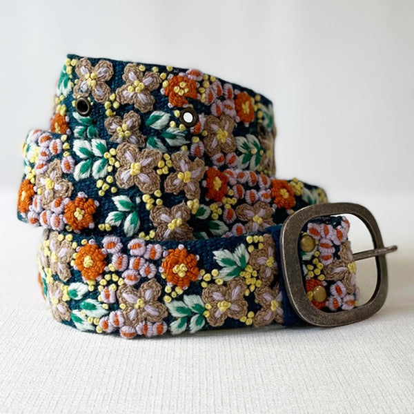 Photo of monochromatic hand-embroidered floral wool belt by Jenny Krauss, made in Peru with lead-free metal buckle. Versatile design with five sets of 2" spaced holes for hip or waist wear, featuring slight stretch for comfort.