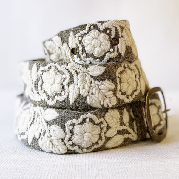 Photo of monochromatic hand-embroidered floral wool belt by Jenny Krauss, made in Peru with lead-free metal buckle. Versatile design with five sets of 2" spaced holes for hip or waist wear, featuring slight stretch for comfort.