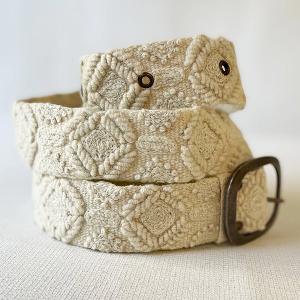 Photo of monochromatic hand-embroidered floral wool belt by Jenny Krauss, made in Peru with lead-free metal buckle. Versatile design with five sets of 2" spaced holes for hip or waist wear, featuring slight stretch for comfort.