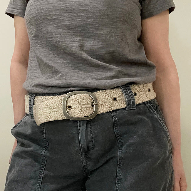 Photo of monochromatic hand-embroidered floral wool belt by Jenny Krauss, made in Peru with lead-free metal buckle. Versatile design with five sets of 2" spaced holes for hip or waist wear, featuring slight stretch for comfort.