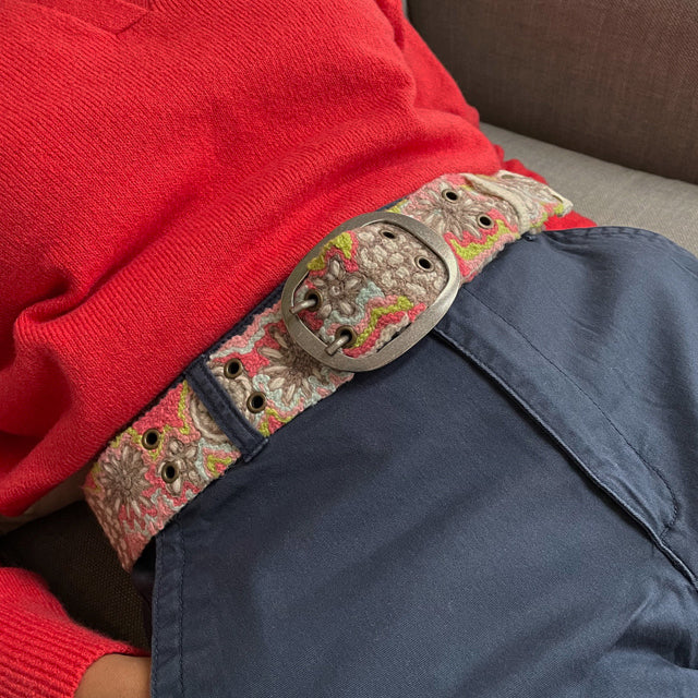 Photo of colorful hand-embroidered floral wool belt by Jenny Krauss, made in Peru with lead-free metal buckle. Versatile design with five sets of 2" spaced holes for hip or waist wear, featuring slight stretch for comfort.
