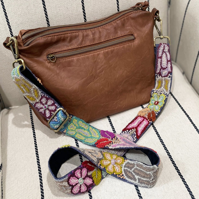 Photo of Jenny Krauss hand-embroidered wool bag strap from Peru. Multi-functional design serves as a camera or guitar strap. Vibrant floral pattern, lead-free metal hardware, and adjustable length for versatile use. Elevate your style with this artisanal accessory.
