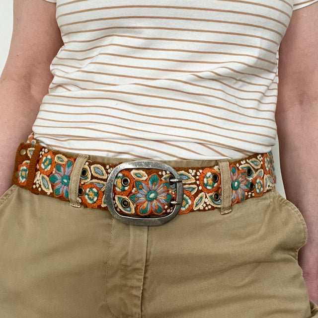 Photo of colorful hand-embroidered floral wool belt by Jenny Krauss, made in Peru with lead-free metal buckle. Versatile design with five sets of 2" spaced holes for hip or waist wear, featuring slight stretch for comfort.
