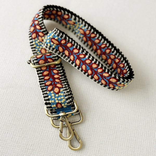 Photo of Jenny Krauss hand-embroidered wool strap from Peru. Multi-functional design serves as a bag or camera strap. Vibrant floral pattern, lead-free metal hardware, and adjustable length for versatile use. Elevate your style with this artisanal accessory.