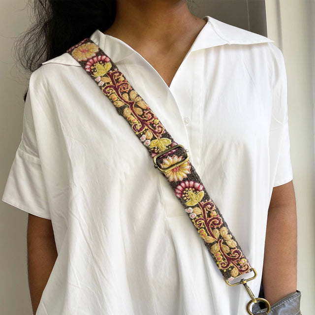 Photo of Jenny Krauss hand-embroidered wool bag strap from Peru. Multi-functional design serves as a camera or guitar strap. Vibrant floral pattern, lead-free metal hardware, and adjustable length for versatile use. Elevate your style with this artisanal accessory.