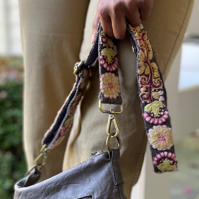 Photo of Jenny Krauss hand-embroidered wool bag strap from Peru. Multi-functional design serves as a camera or guitar strap. Vibrant floral pattern, lead-free metal hardware, and adjustable length for versatile use. Elevate your style with this artisanal accessory.