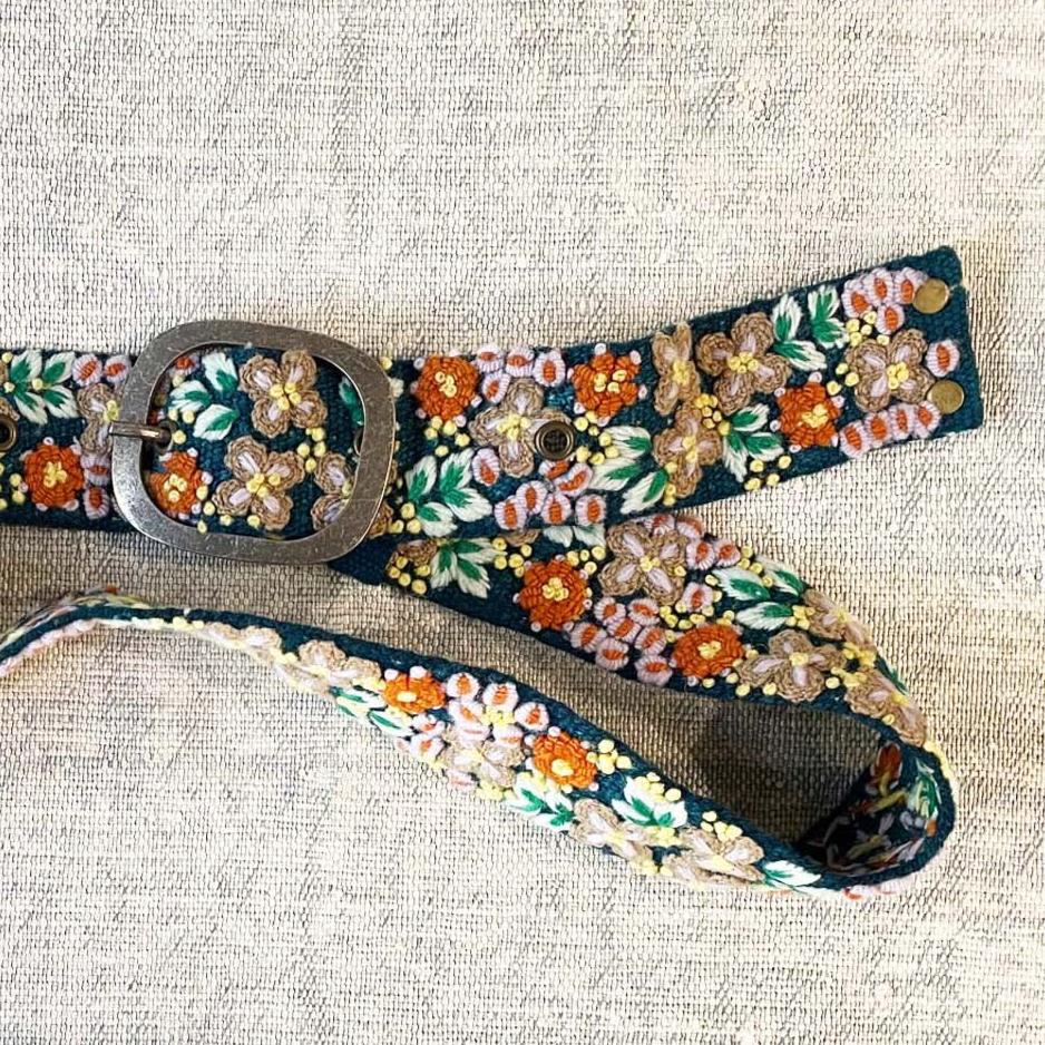 Photo of monochromatic hand-embroidered floral wool belt by Jenny Krauss, made in Peru with lead-free metal buckle. Versatile design with five sets of 2" spaced holes for hip or waist wear, featuring slight stretch for comfort.