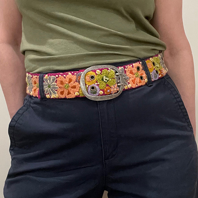 Photo of colorful hand-embroidered floral wool belt by Jenny Krauss, made in Peru with lead-free metal buckle. Versatile design with five sets of 2" spaced holes for hip or waist wear, featuring slight stretch for comfort.