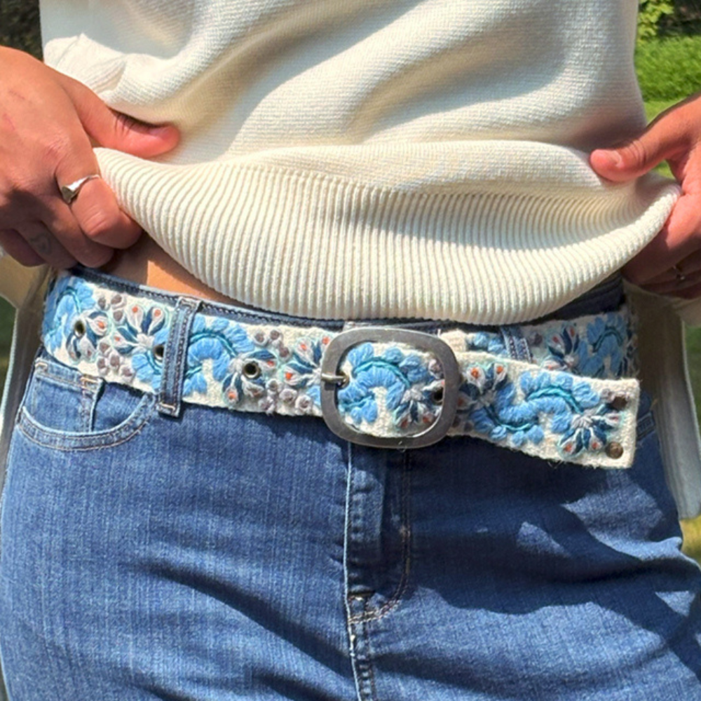 Close-up of a person wearing a white sweater and blue jeans with an ornate belt.