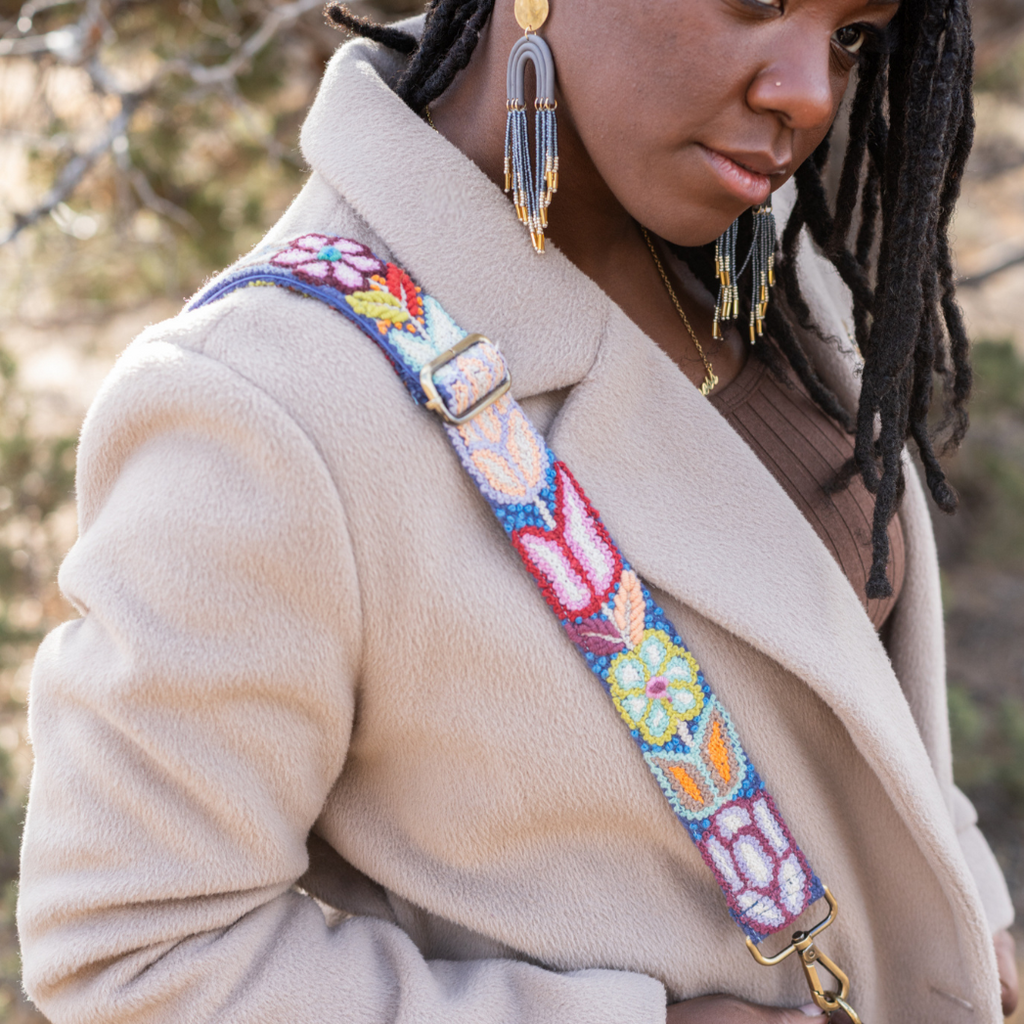Photo of Jenny Krauss hand-embroidered wool strap from Peru. Multi-functional design serves as a bag or camera strap. Vibrant floral pattern, lead-free metal hardware, and adjustable length for versatile use. Elevate your style with this artisanal accessory.