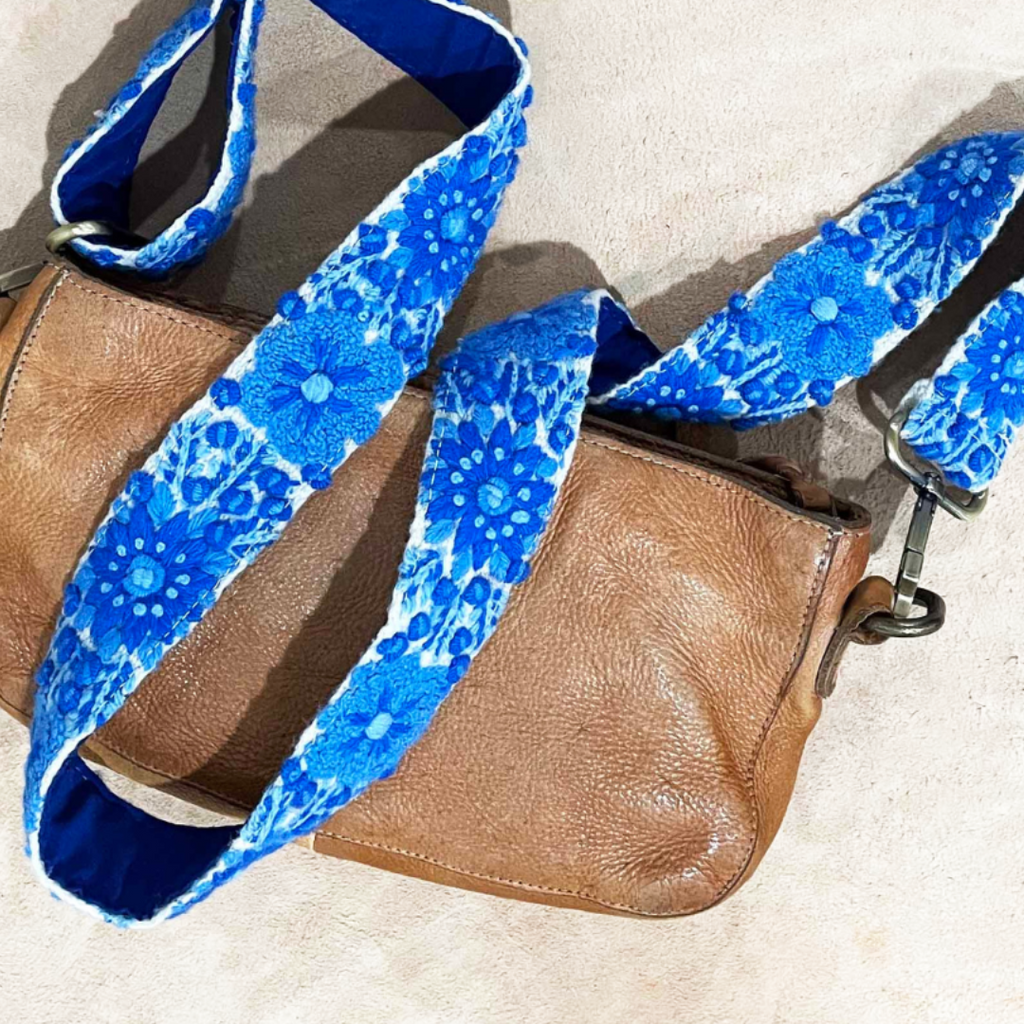 Photo of Jenny Krauss hand-embroidered wool strap from Peru. Multi-functional design serves as a bag or camera strap. Vibrant floral pattern, lead-free metal hardware, and adjustable length for versatile use. Elevate your style with this artisanal accessory.