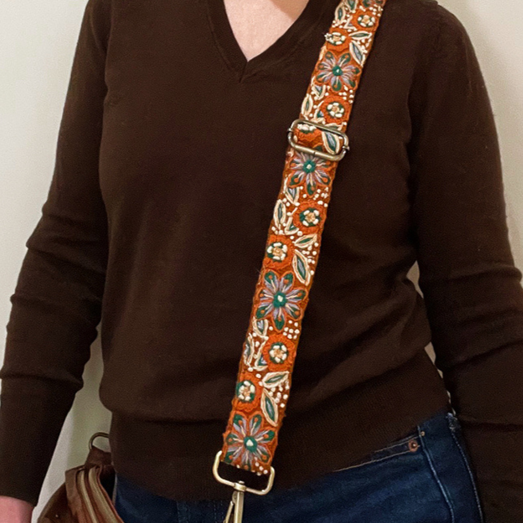 xPhoto of Jenny Krauss hand-embroidered wool strap from Peru. Multi-functional design serves as a bag or camera strap. Vibrant floral pattern, lead-free metal hardware, and adjustable length for versatile use. Elevate your style with this artisanal accessory.