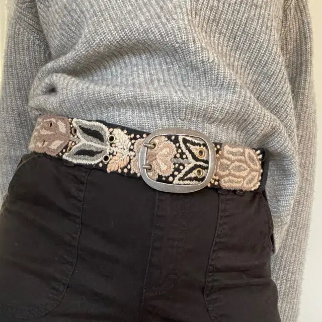 Photo of monochromatic hand-embroidered floral wool belt by Jenny Krauss, made in Peru with lead-free metal buckle. Versatile design with five sets of 2" spaced holes for hip or waist wear, featuring slight stretch for comfort.