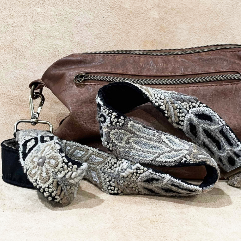 Photo of Jenny Krauss hand-embroidered wool strap from Peru. Multi-functional design serves as a camera or bag strap. Monochromatic floral pattern, lead-free metal hardware, and adjustable length for versatile use. Elevate your style with this artisanal accessory.