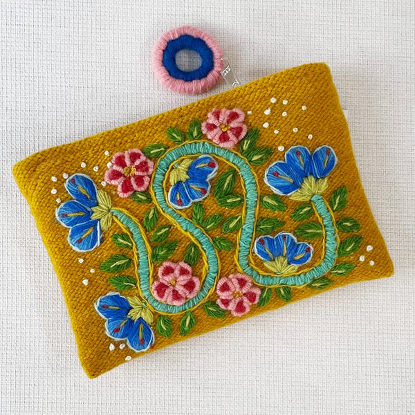 Photo of Jenny Krauss embroidered wool pouch, multi-functional travel accessory. Handcrafted with 100% wool, cotton lining, and sturdy metal zipper. Versatile for use as a wallet, clutch, or keepsake bag. Measures 5.5" L x 8" W. Designed in the U.S.A. and handmade in Peru by skilled artisans.