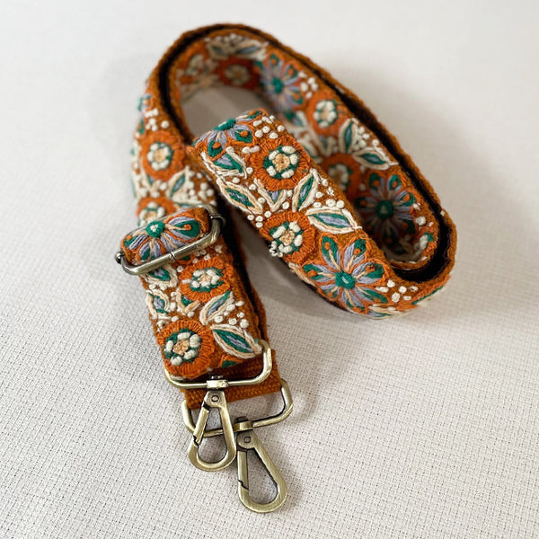 Photo of Jenny Krauss hand-embroidered wool bag strap from Peru. Multi-functional design serves as a camera or guitar strap. Vibrant floral pattern, lead-free metal hardware, and adjustable length for versatile use. Elevate your style with this artisanal accessory.