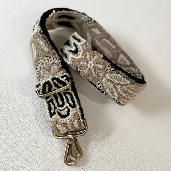 Photo of Jenny Krauss hand-embroidered wool bag strap from Peru. Multi-functional design serves as a camera or guitar strap. Monochromatic floral pattern, lead-free metal hardware, and adjustable length for versatile use. Elevate your style with this artisanal accessory.