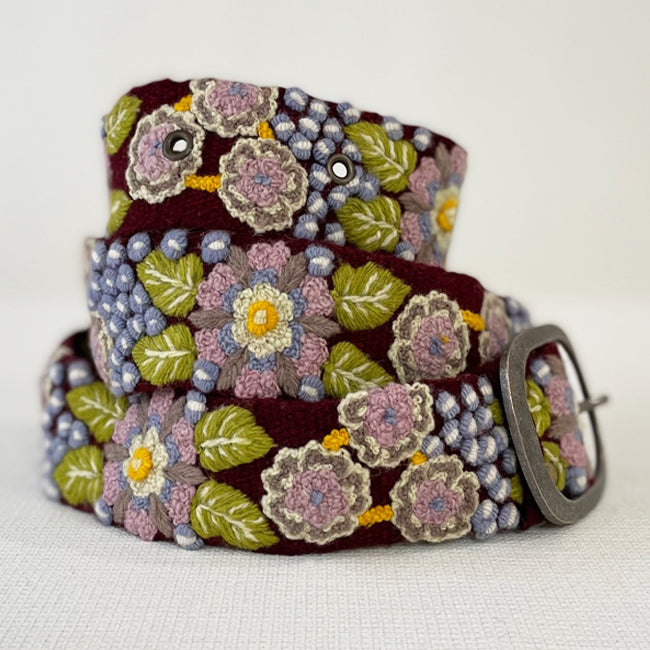 Photo of colorful hand-embroidered floral wool belt by Jenny Krauss, made in Peru with lead-free metal buckle. Versatile design with five sets of 2" spaced holes for hip or waist wear, featuring slight stretch for comfort.