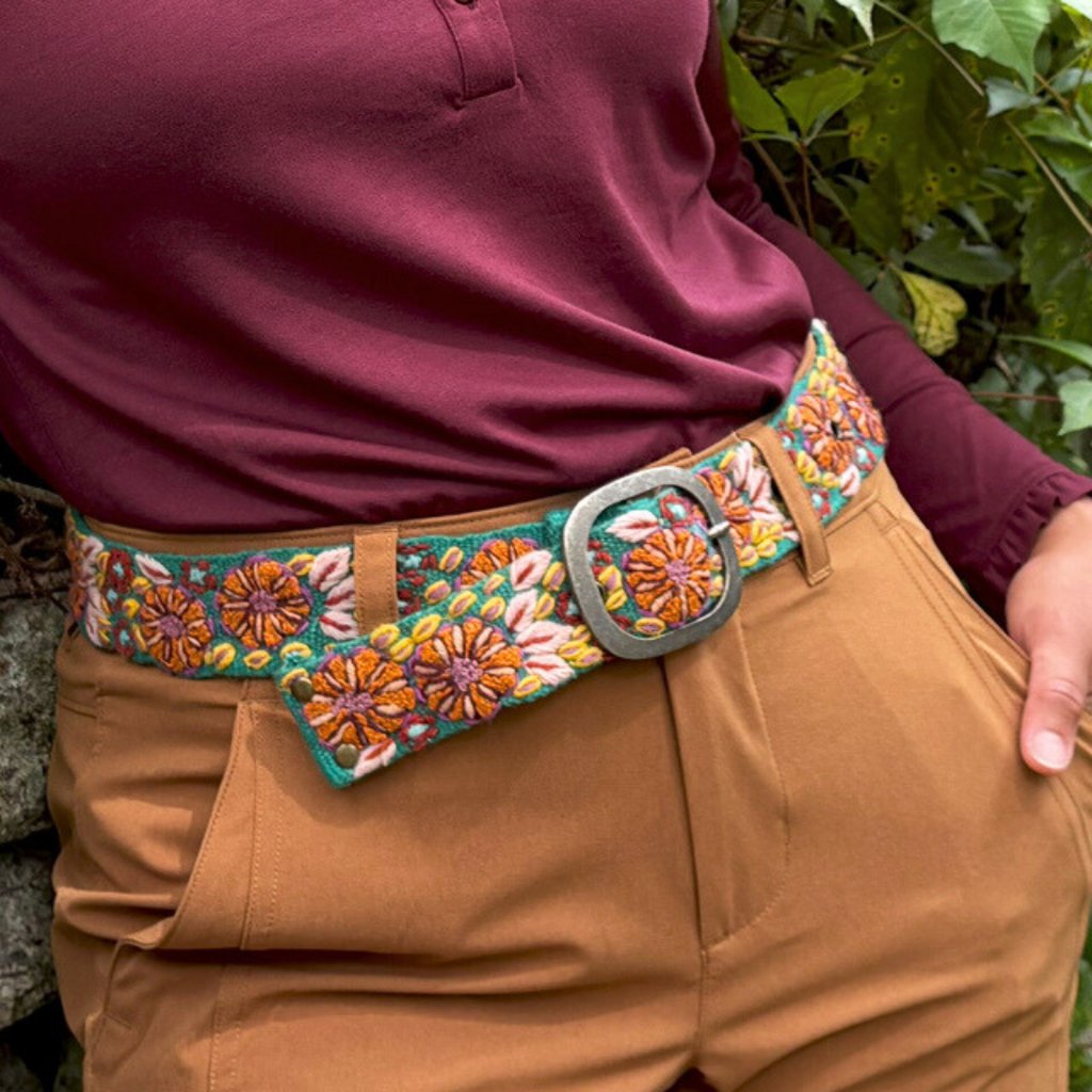 Photo of woman wearing colorful hand-embroidered floral wool belt by Jenny Krauss, made in Peru with lead-free metal buckle. Versatile design with five sets of 2" spaced holes for hip or waist wear, featuring slight stretch for comfort.