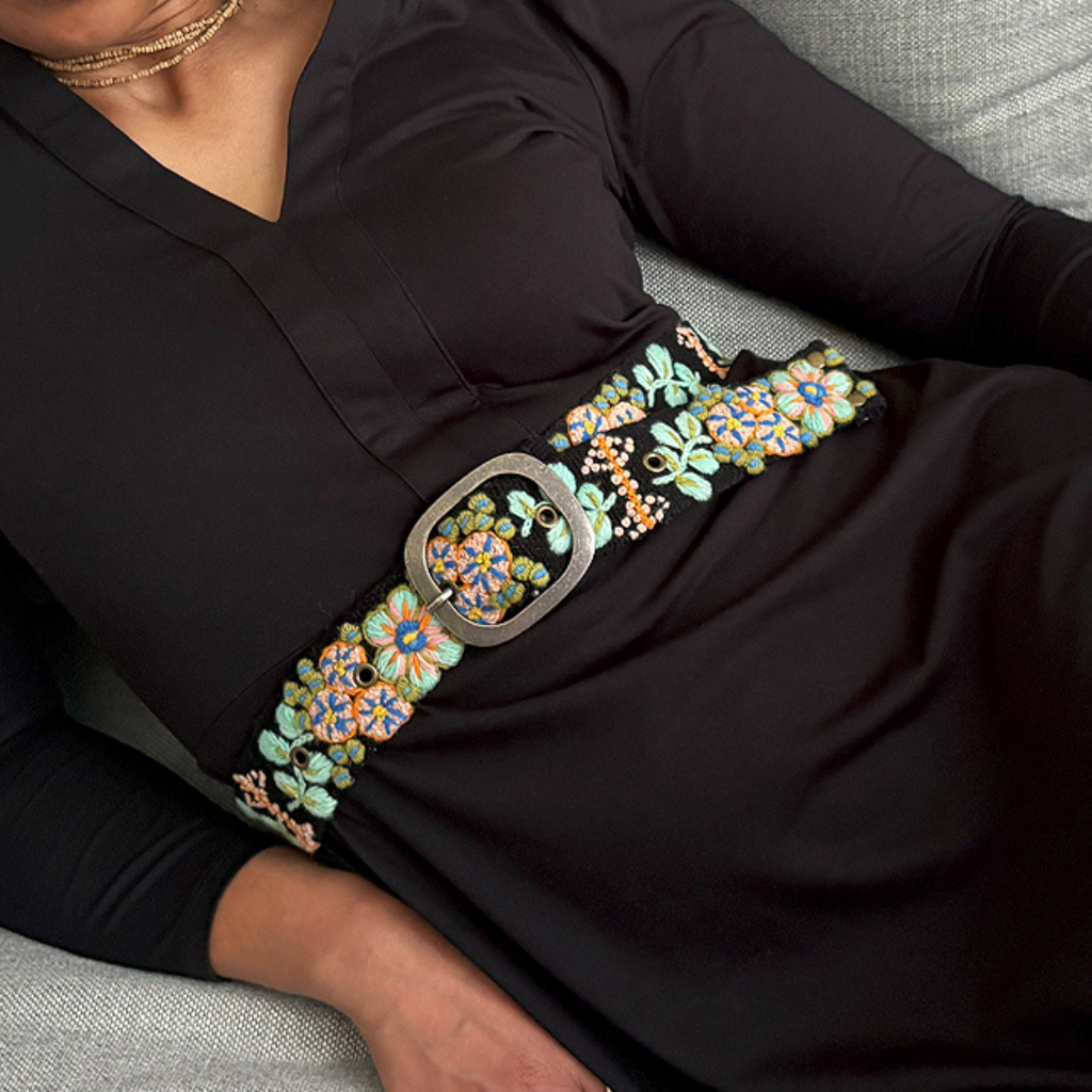 Photo of woman wearing colorful hand-embroidered floral wool belt by Jenny Krauss, made in Peru with lead-free metal buckle. Versatile design with five sets of 2" spaced holes for hip or waist wear, featuring slight stretch for comfort.