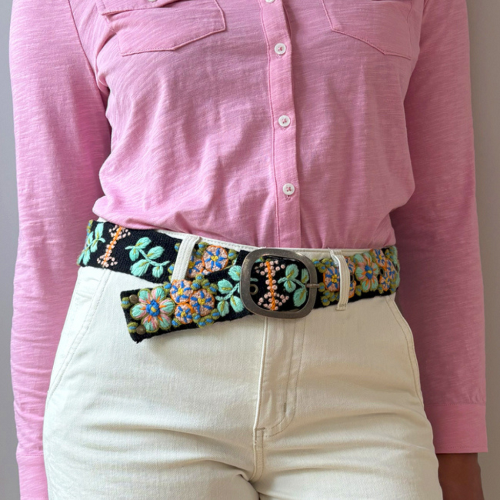 Photo of woman wearing colorful hand-embroidered floral wool belt by Jenny Krauss, made in Peru with lead-free metal buckle. Versatile design with five sets of 2" spaced holes for hip or waist wear, featuring slight stretch for comfort.