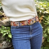 Person wearing a floral belt with a stone wall and greenery in the background
