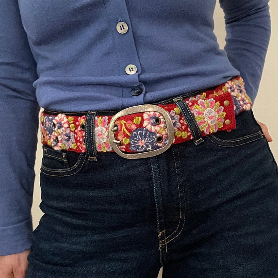 Photo of colorful hand-embroidered floral wool belt by Jenny Krauss, made in Peru with lead-free metal buckle. Versatile design with five sets of 2" spaced holes for hip or waist wear, featuring slight stretch for comfort.