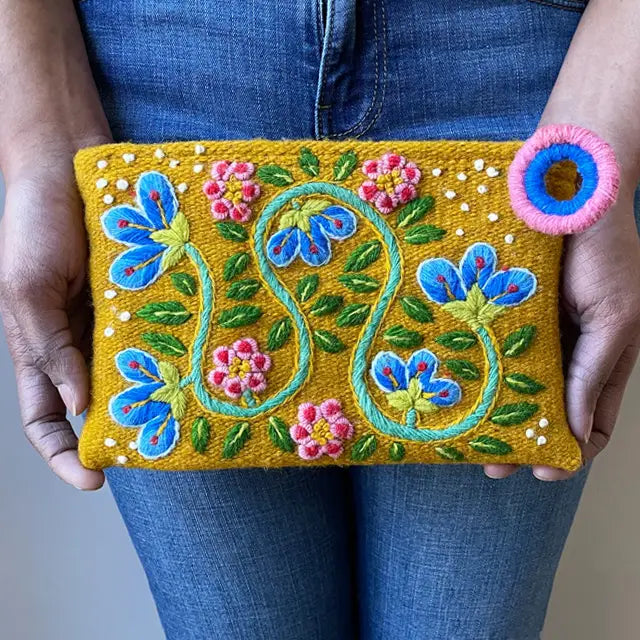Photo of Jenny Krauss embroidered wool pouch, multi-functional travel accessory. Handcrafted with 100% wool, cotton lining, and sturdy metal zipper. Versatile for use as a wallet, clutch, or keepsake bag. Measures 5.5" L x 8" W. Designed in the U.S.A. and handmade in Peru by skilled artisans.