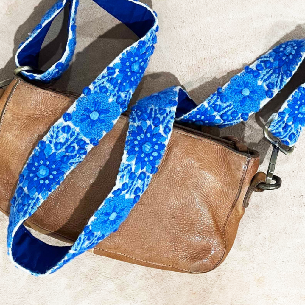 Photo of Jenny Krauss hand-embroidered wool bag strap from Peru. Multi-functional design serves as a camera or guitar strap. Vibrant floral pattern, lead-free metal hardware, and adjustable length for versatile use. Elevate your style with this artisanal accessory.