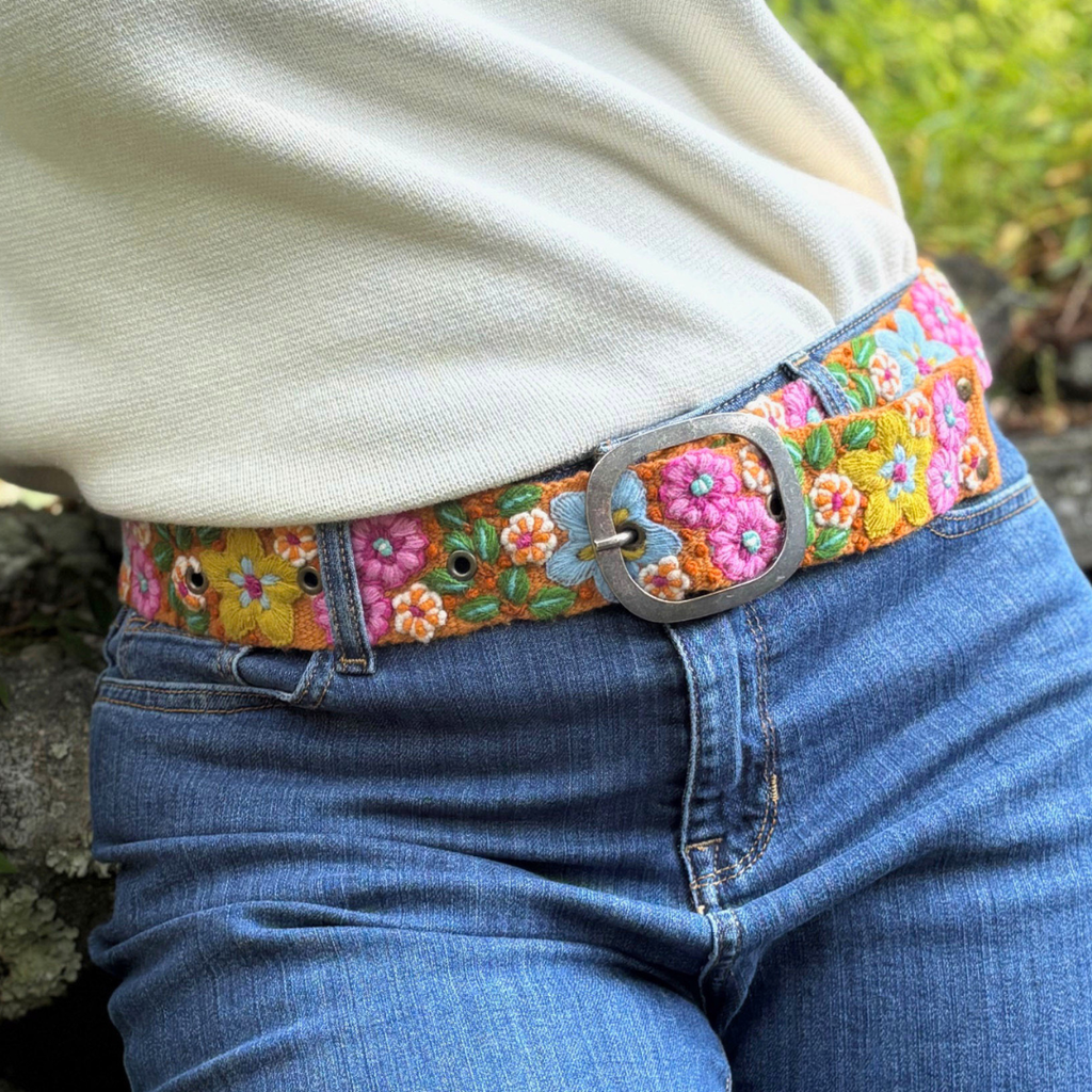Person wearing a colorful floral belt with blue jeans outdoors.