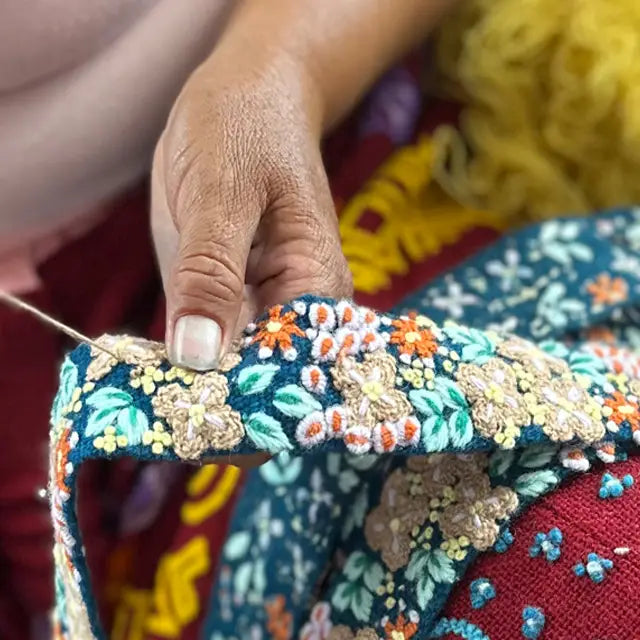 Photo of colorful hand-embroidered floral wool belt by Jenny Krauss being handcrafted by arisan. Made in Peru with lead-free metal buckle. Versatile design with five sets of 2" spaced holes for hip or waist wear, featuring slight stretch for comfort.