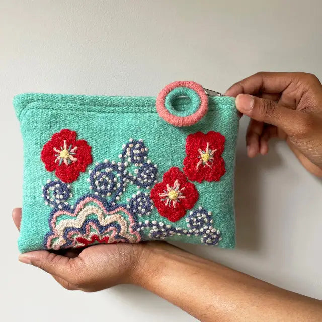  Photo of Jenny Krauss embroidered wool pouch, multi-functional travel accessory. Handcrafted with 100% wool, cotton lining, and sturdy metal zipper. Versatile for use as a wallet, clutch, or keepsake bag. Measures 5.5" L x 8" W. Designed in the U.S.A. and handmade in Peru by skilled artisans.