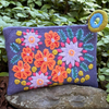 Colorful embroidered floral pouch on a stone with green foliage in the background