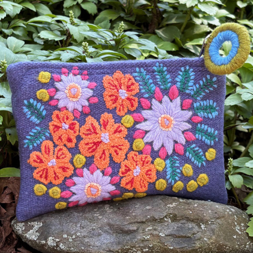 Colorful embroidered floral pouch on a stone with green foliage in the background